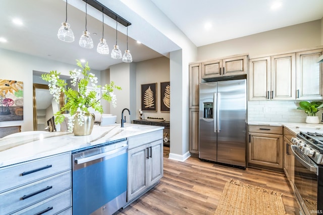 kitchen featuring stainless steel appliances, sink, light stone counters, wood-type flooring, and decorative backsplash