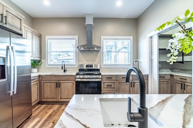 kitchen featuring light wood-type flooring, appliances with stainless steel finishes, wall chimney exhaust hood, and light stone counters