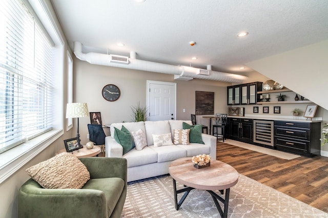 living room featuring hardwood / wood-style flooring, bar, a textured ceiling, and wine cooler