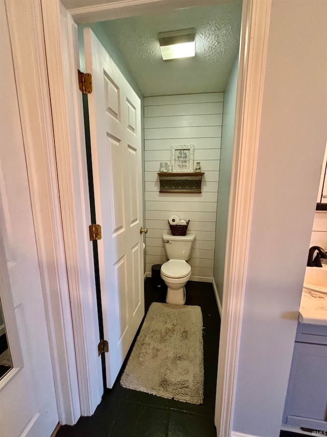 bathroom featuring toilet, wooden walls, a textured ceiling, and tile patterned floors