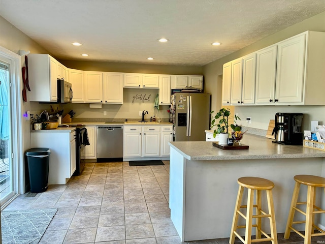 kitchen with a kitchen bar, stainless steel appliances, white cabinets, kitchen peninsula, and sink