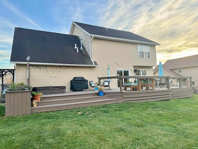 back house at dusk with a deck, a yard, and a hot tub