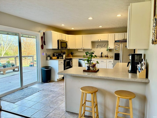 kitchen featuring white cabinets, kitchen peninsula, appliances with stainless steel finishes, and a breakfast bar area