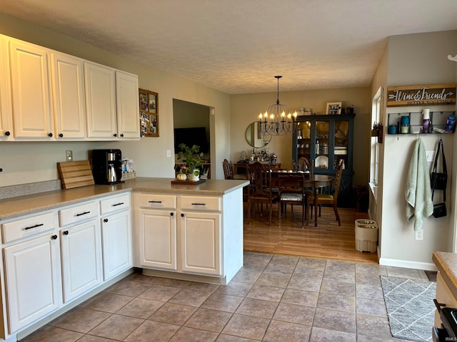 kitchen with pendant lighting, an inviting chandelier, light hardwood / wood-style floors, white cabinets, and kitchen peninsula