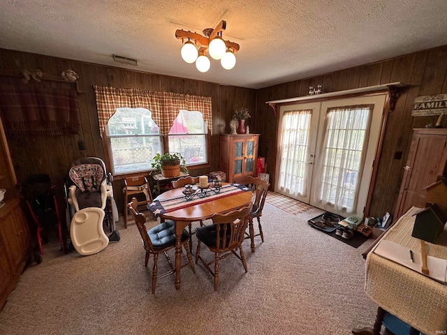 dining room with wood walls, a textured ceiling, carpet flooring, and french doors