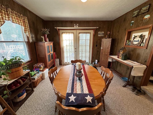 carpeted dining area featuring a textured ceiling, wooden walls, french doors, and plenty of natural light