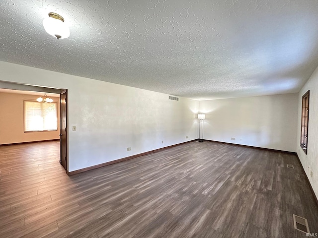 empty room featuring a textured ceiling, a notable chandelier, and dark hardwood / wood-style floors