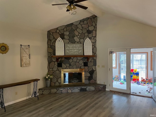 unfurnished living room featuring ceiling fan, hardwood / wood-style flooring, a stone fireplace, and vaulted ceiling with beams