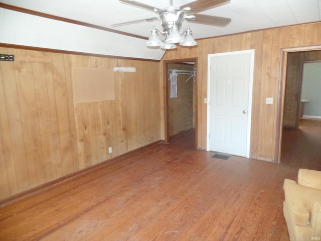 unfurnished bedroom with wood-type flooring, wooden walls, ceiling fan, and a closet