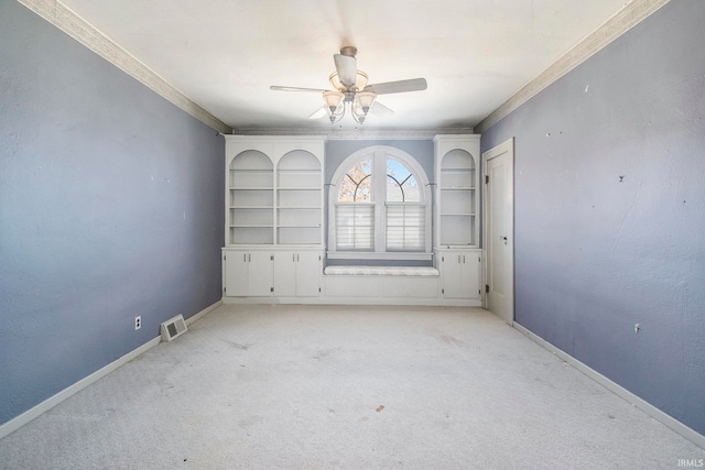 spare room with built in shelves, ceiling fan, light colored carpet, and ornamental molding