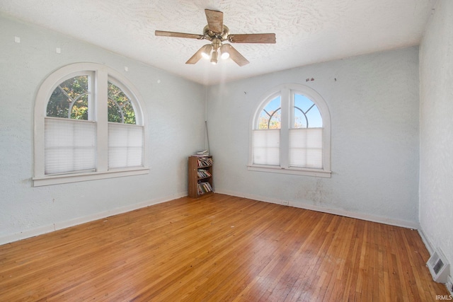 spare room with ceiling fan, wood-type flooring, plenty of natural light, and a textured ceiling