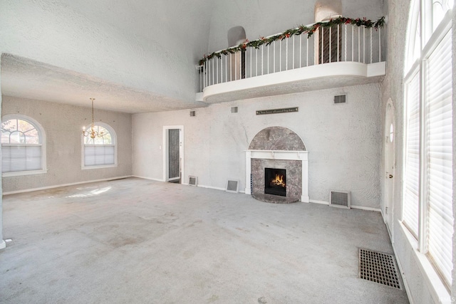 unfurnished living room with carpet, a textured ceiling, a notable chandelier, and a towering ceiling