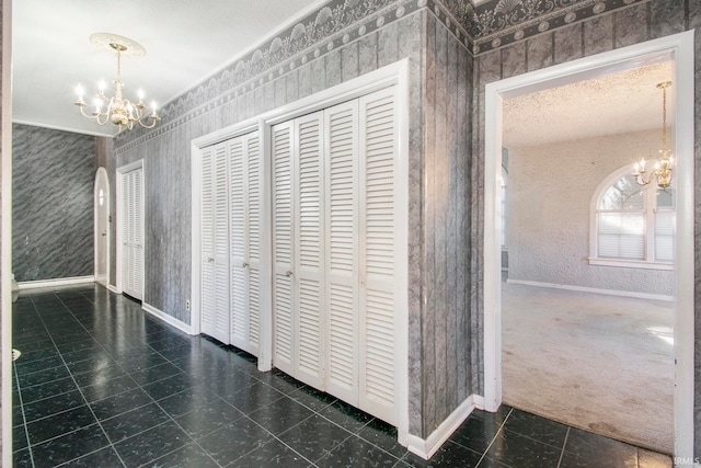 hall with ornamental molding, an inviting chandelier, a textured ceiling, and dark carpet