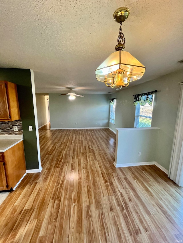 unfurnished dining area with ceiling fan with notable chandelier, a textured ceiling, and light hardwood / wood-style flooring