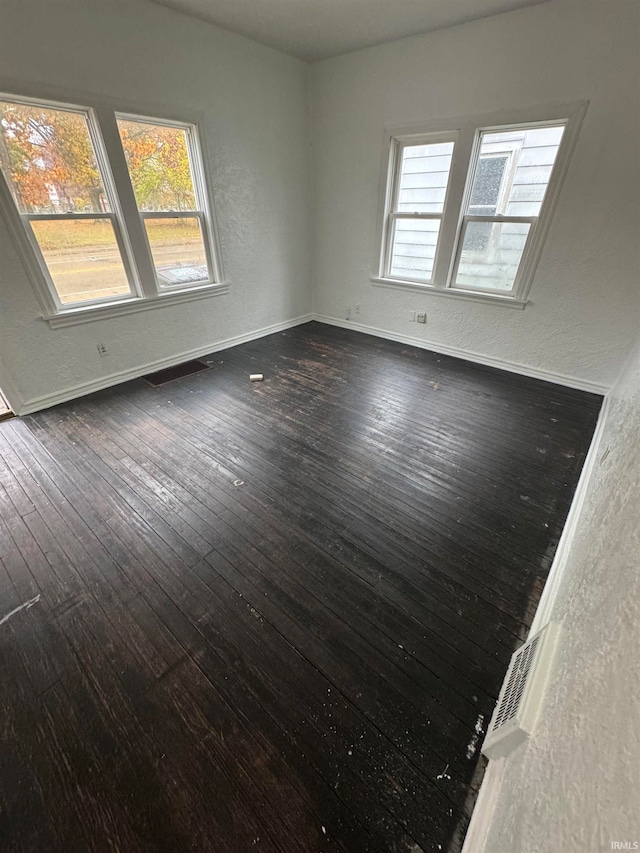 empty room with dark hardwood / wood-style floors and plenty of natural light