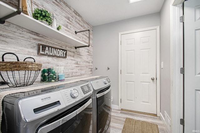 laundry area featuring light wood-type flooring, wooden walls, and washing machine and clothes dryer