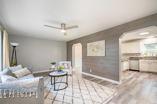 living room with wood walls, ceiling fan, sink, and light hardwood / wood-style floors