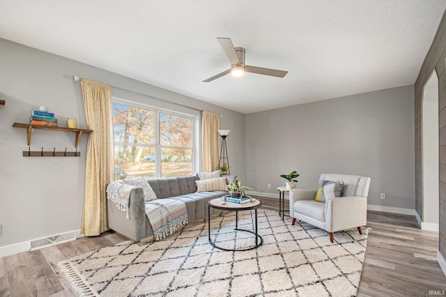 living room with ceiling fan, a textured ceiling, and light wood-type flooring