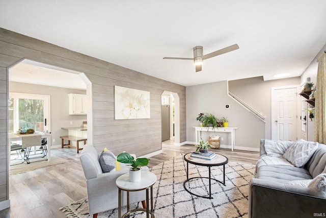 living room with wood walls, ceiling fan, and light hardwood / wood-style floors