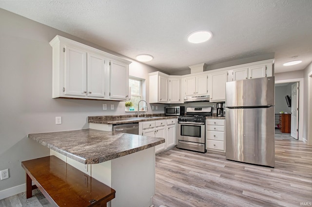 kitchen with stainless steel appliances, light wood-type flooring, a textured ceiling, white cabinets, and kitchen peninsula