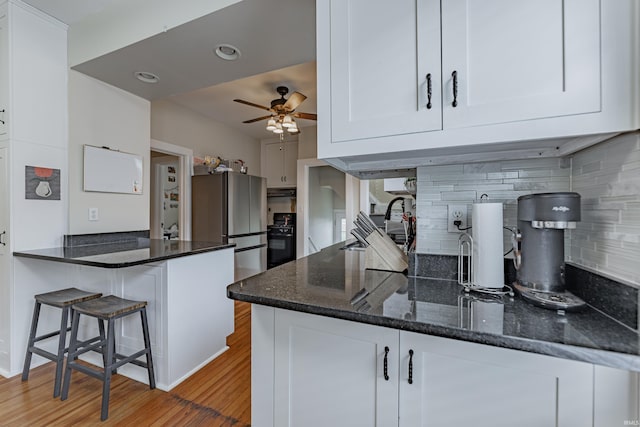 kitchen featuring tasteful backsplash, dark stone countertops, white cabinets, fridge, and kitchen peninsula