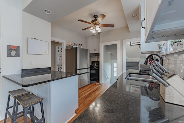 kitchen featuring white cabinetry, stainless steel fridge, dark stone countertops, and black range with gas stovetop