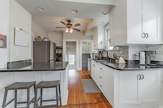 kitchen featuring appliances with stainless steel finishes, white cabinetry, sink, dark stone counters, and kitchen peninsula