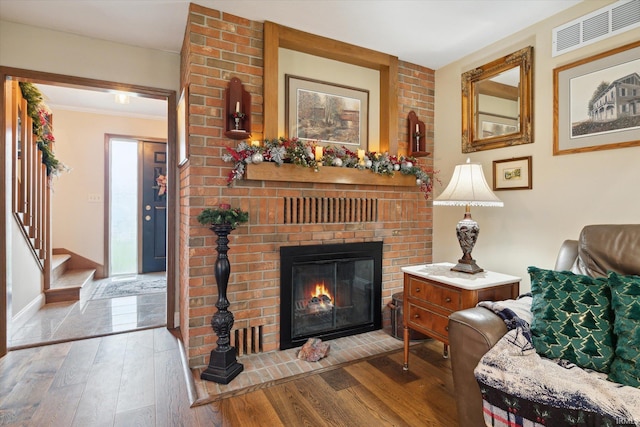 living room with hardwood / wood-style floors, a brick fireplace, and crown molding