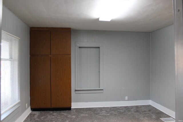 unfurnished bedroom with wood walls and dark colored carpet