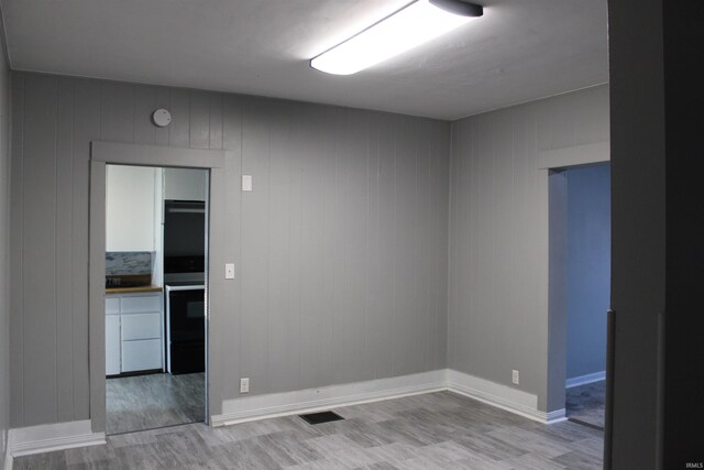 unfurnished room with wooden walls and light wood-type flooring