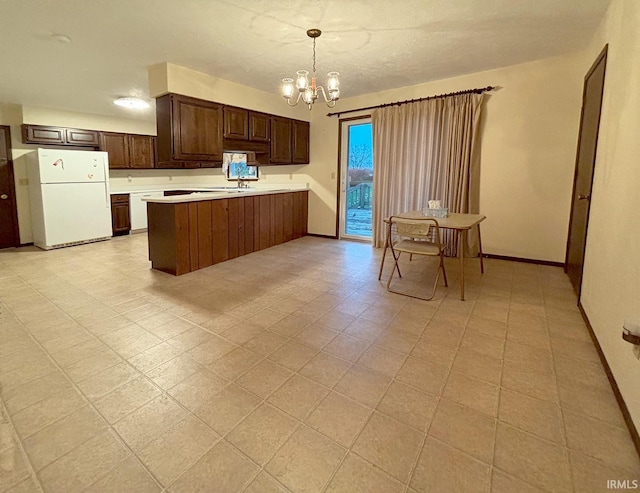 kitchen with white refrigerator, kitchen peninsula, dark brown cabinetry, a chandelier, and pendant lighting