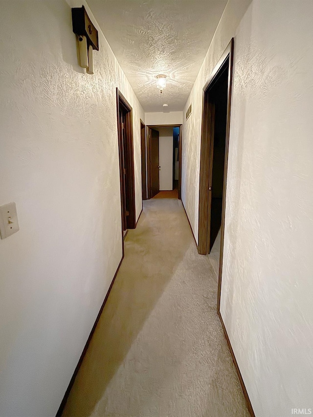 corridor with light colored carpet and a textured ceiling