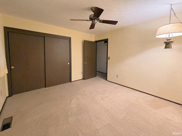 unfurnished bedroom featuring ceiling fan, light colored carpet, a textured ceiling, and a closet