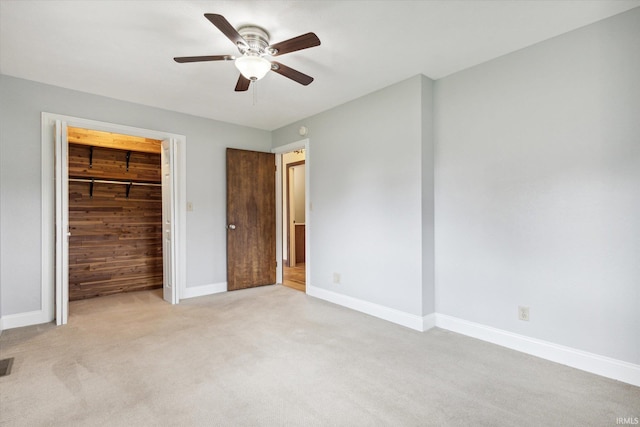 unfurnished bedroom with light carpet, ceiling fan, wooden walls, and a closet