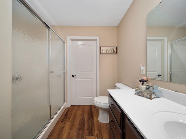 bathroom featuring toilet, vanity, hardwood / wood-style flooring, and a shower with shower door