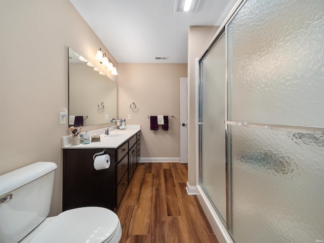 bathroom with hardwood / wood-style flooring, a shower with shower door, vanity, and toilet