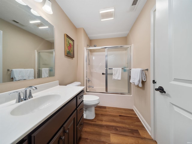 full bathroom with hardwood / wood-style floors, vanity, combined bath / shower with glass door, and toilet