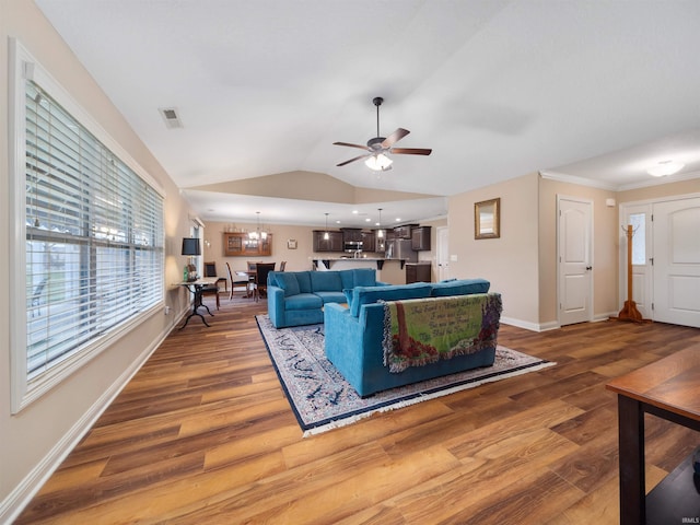 living room with ceiling fan with notable chandelier, hardwood / wood-style flooring, and vaulted ceiling