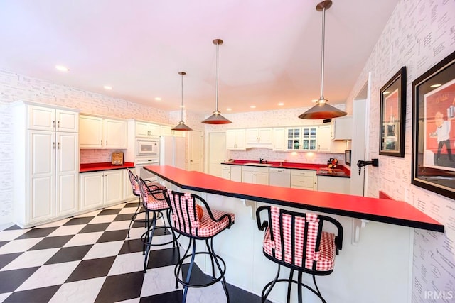 kitchen featuring backsplash, pendant lighting, sink, a kitchen breakfast bar, and white appliances