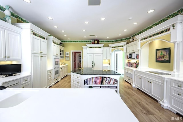 kitchen featuring dark stone counters, white cabinetry, light hardwood / wood-style flooring, white appliances, and a center island