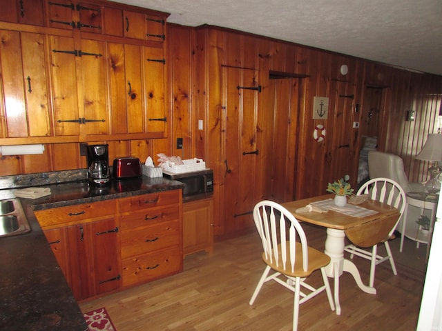 dining area featuring light hardwood / wood-style flooring, wood walls, and a textured ceiling