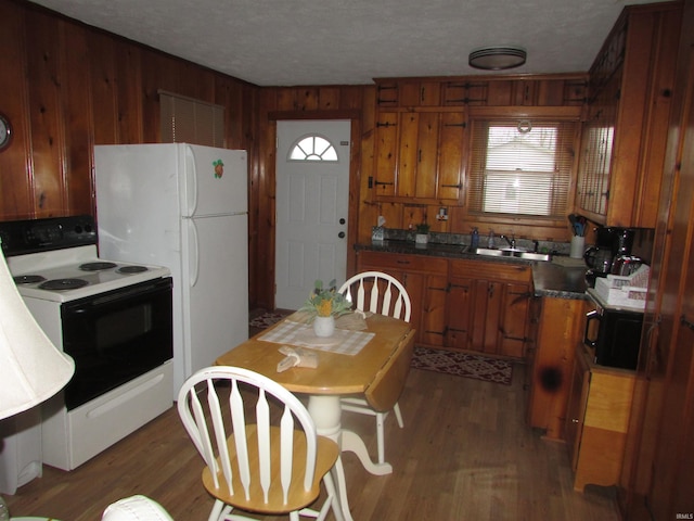 kitchen with a textured ceiling, wood walls, sink, dark wood-type flooring, and white appliances