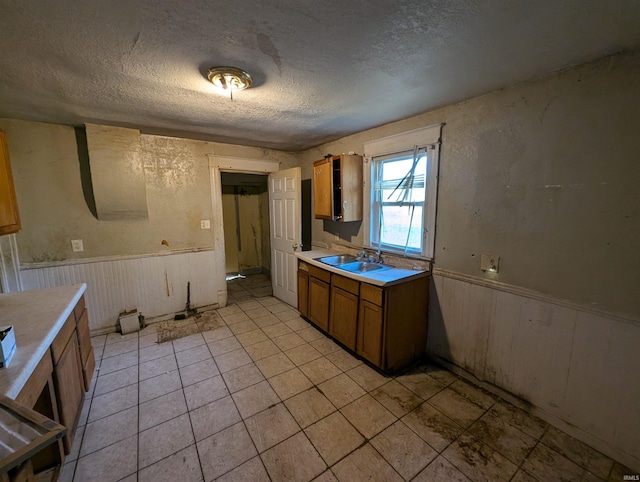 kitchen with sink, wooden walls, a textured ceiling, and light tile patterned flooring