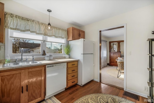 kitchen with hanging light fixtures, white appliances, sink, and dark wood-type flooring