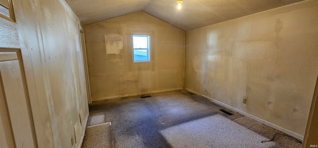 spare room featuring vaulted ceiling, carpet flooring, and a textured ceiling