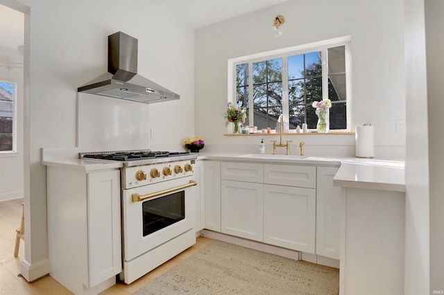 kitchen featuring white cabinetry, high end white range, wall chimney range hood, and sink