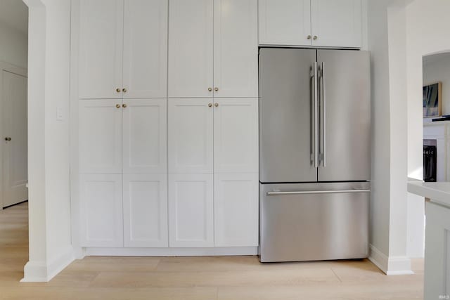 kitchen with stainless steel refrigerator, white cabinetry, and light hardwood / wood-style flooring