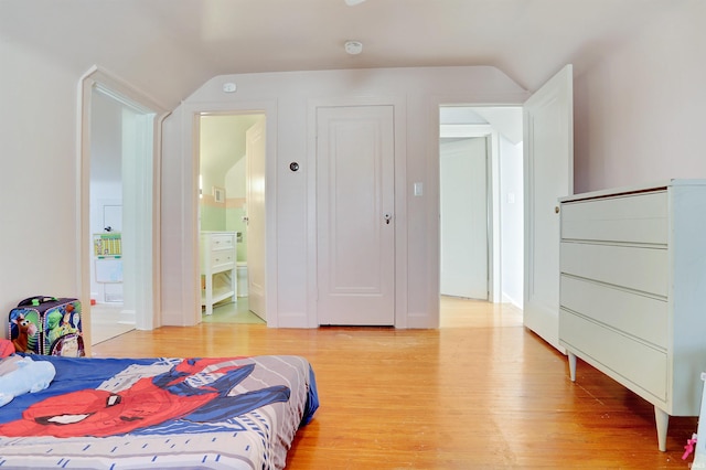 bedroom with hardwood / wood-style floors, vaulted ceiling, and ensuite bath