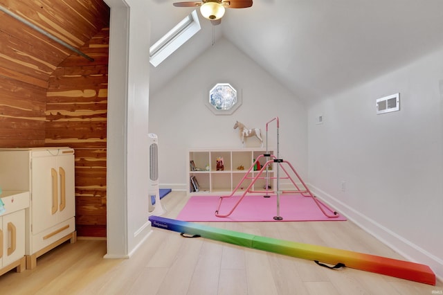 recreation room with wooden walls, vaulted ceiling with skylight, ceiling fan, and hardwood / wood-style flooring