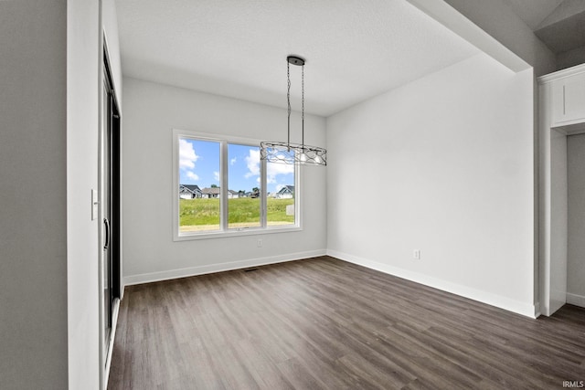 unfurnished dining area featuring a textured ceiling, a notable chandelier, and dark hardwood / wood-style floors